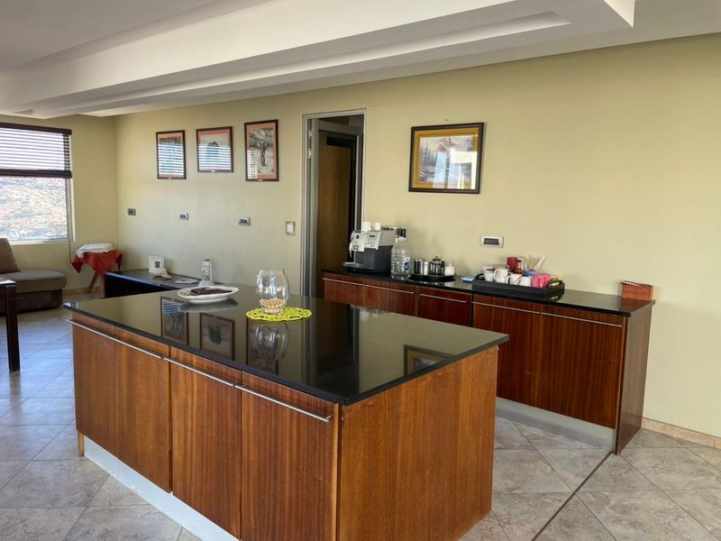 A functional kitchen area featuring a large central island with dark granite countertops and wood cabinetry, complemented by tiled flooring and recessed ceiling lighting.