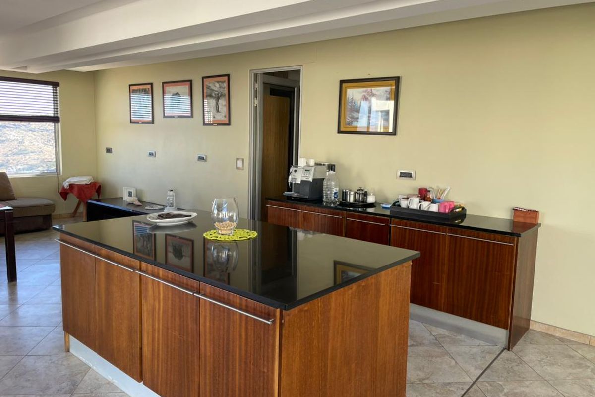 A functional kitchen area featuring a large central island with dark granite countertops and wood cabinetry, complemented by tiled flooring and recessed ceiling lighting.
