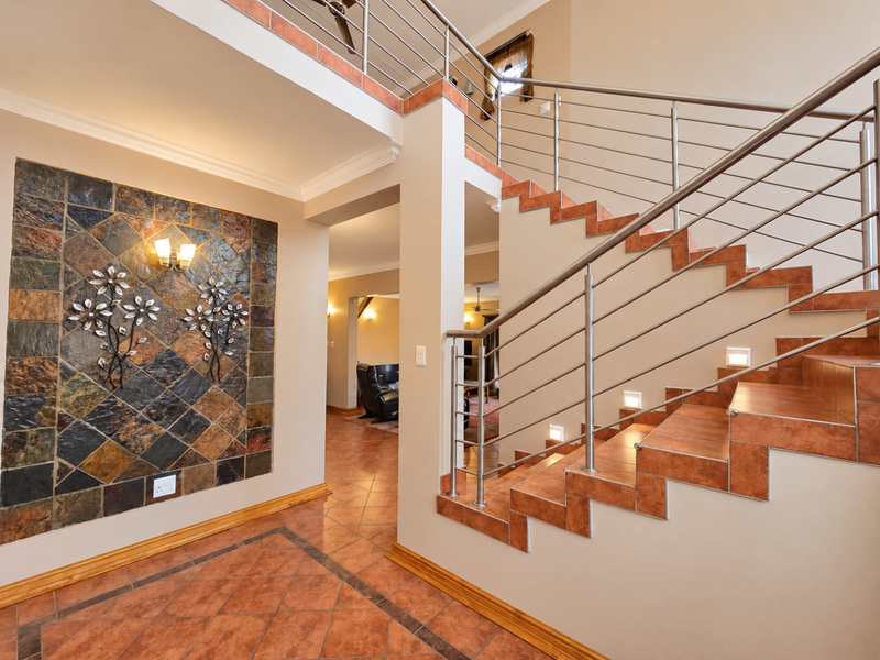Spacious entrance hall featuring a tiled staircase with stainless steel balustrades, accent lighting, and a decorative stone feature wall.