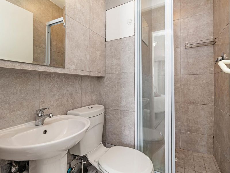 A compact, modern bathroom featuring a pedestal basin, toilet, and a glass-enclosed shower with neutral floor-to-ceiling tiling.