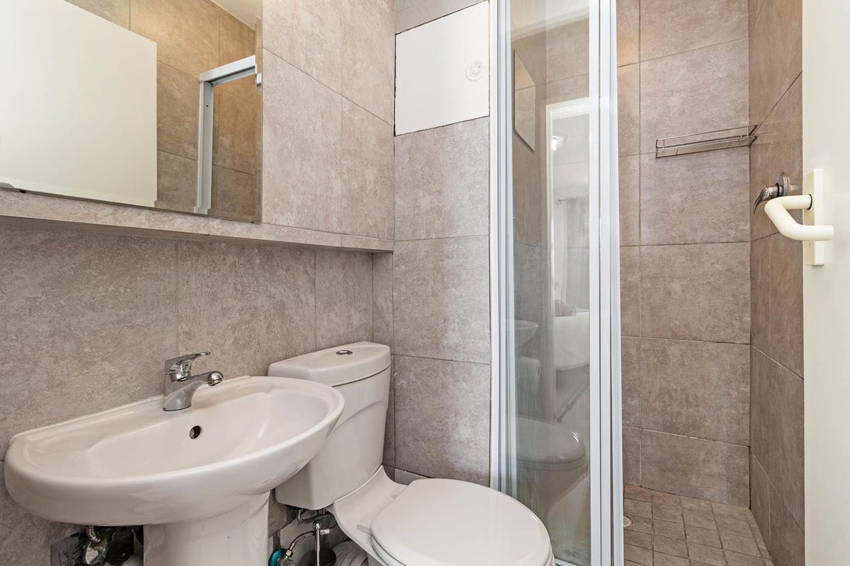 A compact, modern bathroom featuring a pedestal basin, toilet, and a glass-enclosed shower with neutral floor-to-ceiling tiling.