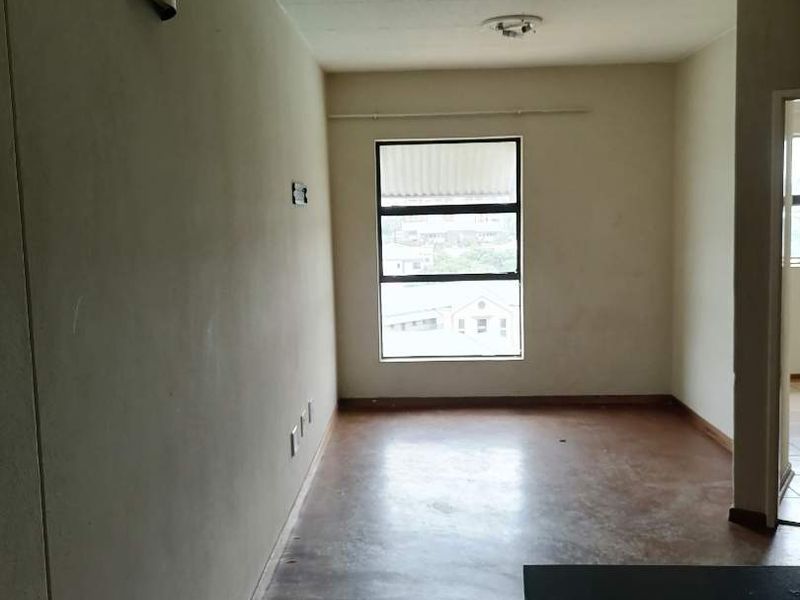 An empty living area featuring a large window, neutral walls, and worn flooring, offering a blank canvas for renovation or interior design updates.