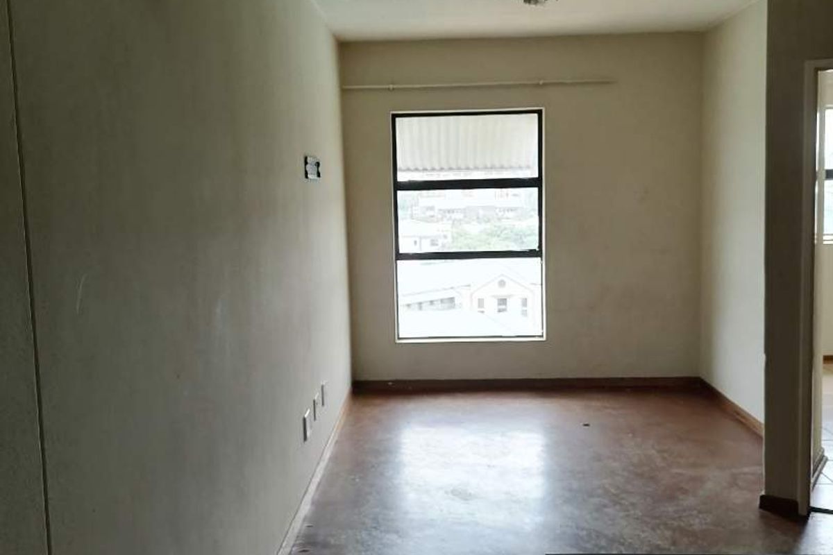 An empty living area featuring a large window, neutral walls, and worn flooring, offering a blank canvas for renovation or interior design updates.