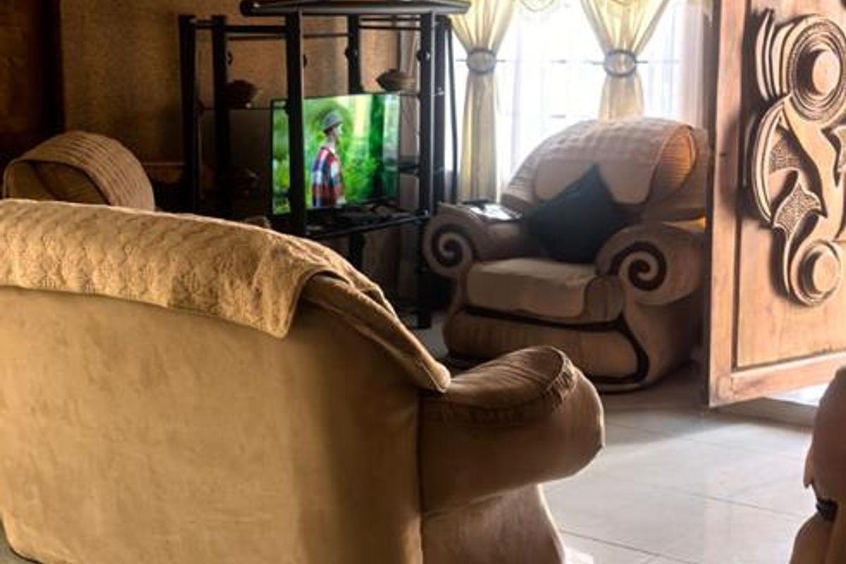 A living room featuring tiled flooring, ornate ceiling detailing, and a carved wooden door, presenting a dated aesthetic.