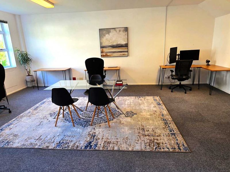 A spacious, well-lit office area featuring neutral carpet flooring and large windows, providing a functional workspace environment.
