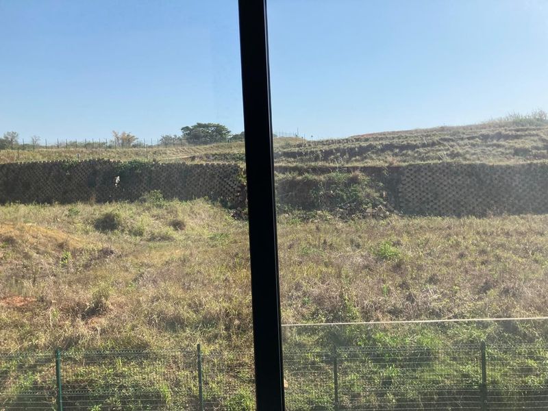 A view from the property looking out over an undeveloped plot with a visible retaining wall and perimeter fencing.