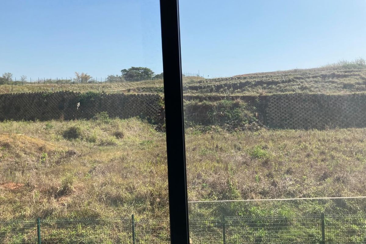 A view from the property looking out over an undeveloped plot with a visible retaining wall and perimeter fencing.