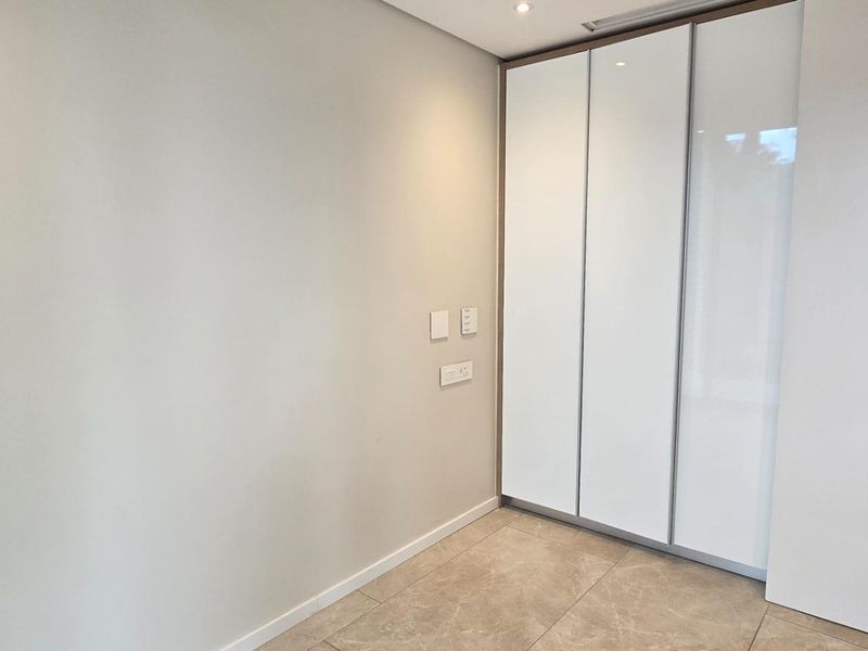A clean, modern bedroom interior featuring high-gloss built-in wardrobes, neutral tiled flooring, and recessed ceiling lighting.