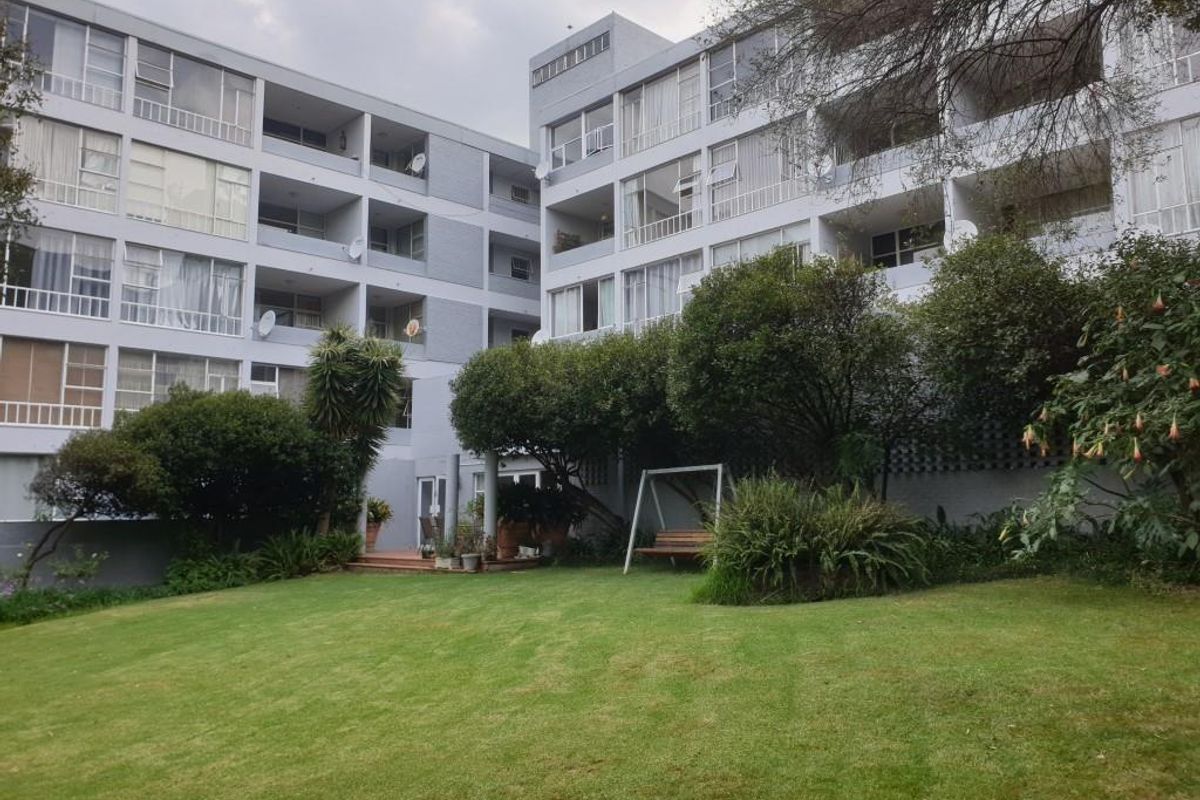 A view of the rear apartment building facade featuring multi-level balconies overlooking a well-maintained communal garden and lawn area.