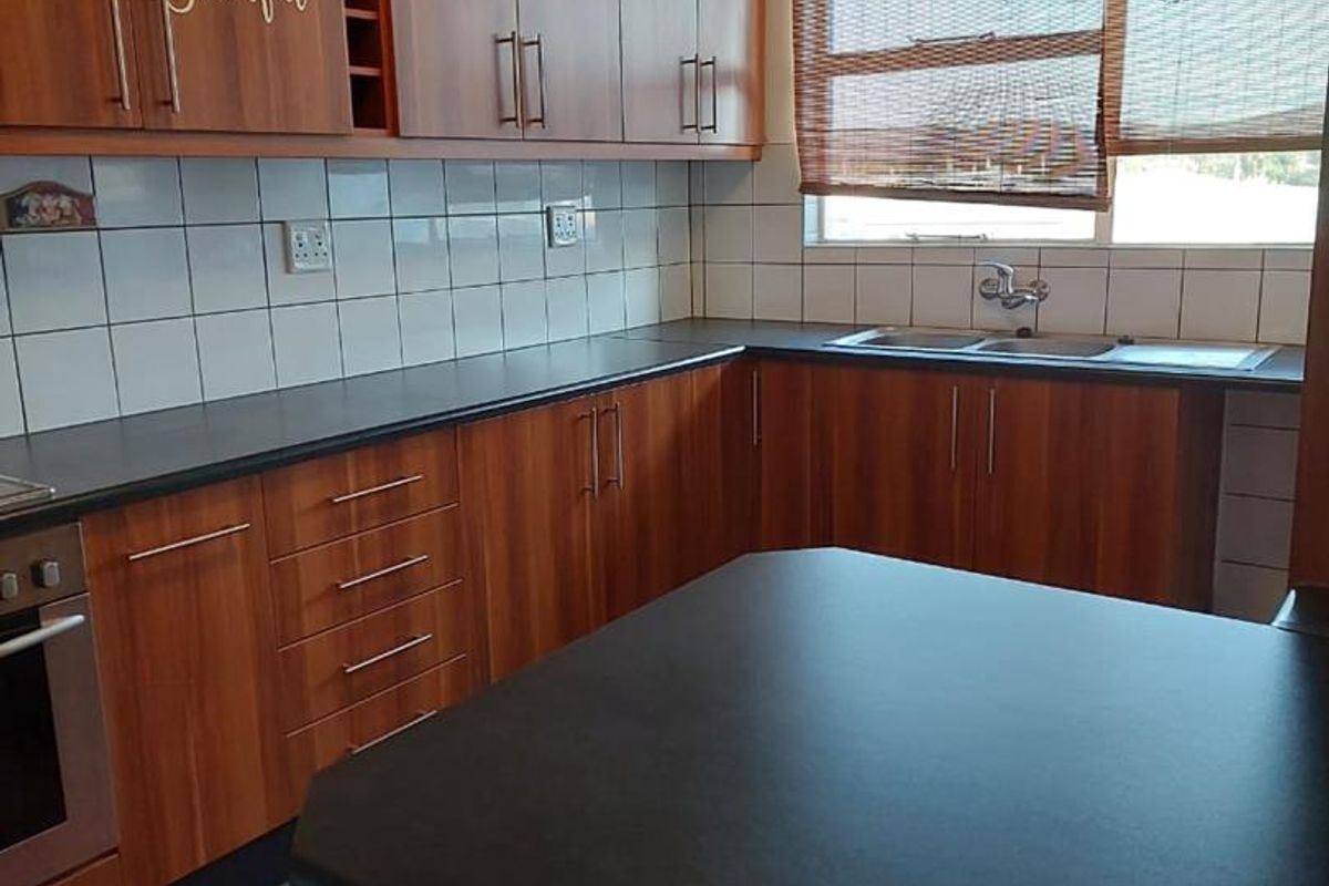 A functional kitchen featuring wood-look cabinetry, dark laminate countertops, tiled backsplash, built-in oven, and a double sink with a window view.