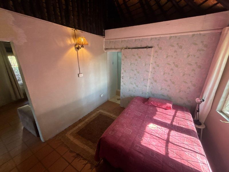 Bedroom featuring a traditional thatch roof, tiled flooring, and a sliding door, with visible wear on the wall finishes.