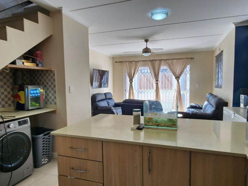Open-plan living area featuring a kitchen with built-in cabinetry, stone countertops, and an integrated laundry space under the staircase, leading to a lounge area.