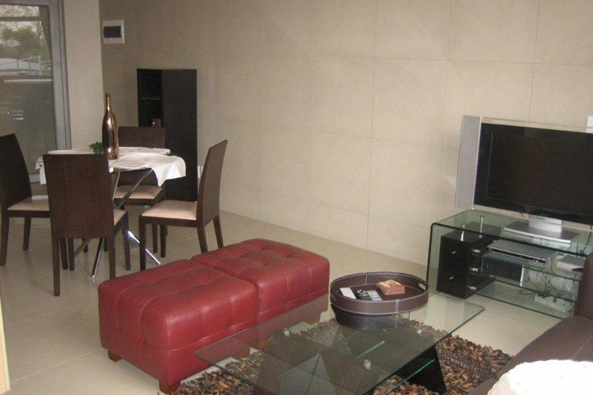 A living room area featuring large format wall tiles, neutral floor tiles, and a sliding glass door leading to an outdoor space.