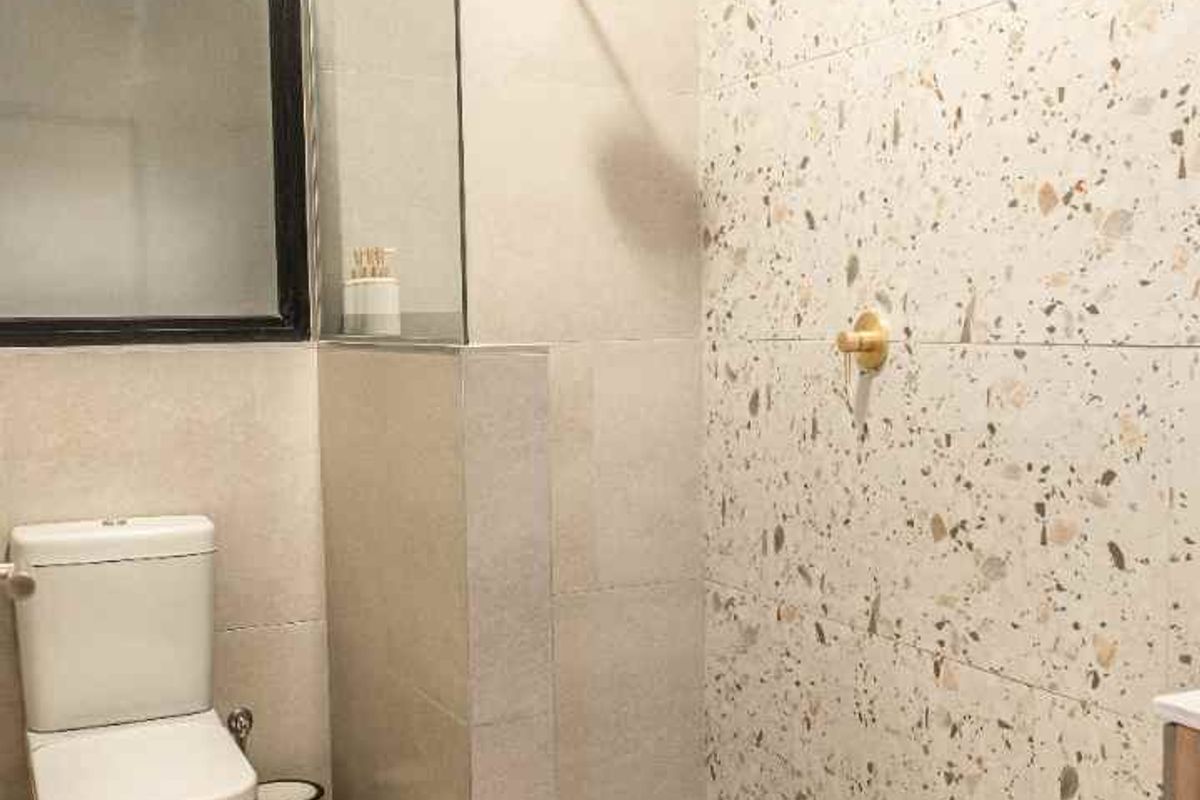 Modern bathroom featuring a walk-in shower with terrazzo-style wall tiles, gold-toned fixtures, and a glass partition.