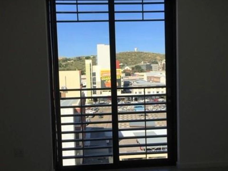 An empty living area featuring tiled flooring, track lighting, and a sliding glass door with an integrated security gate overlooking the city.