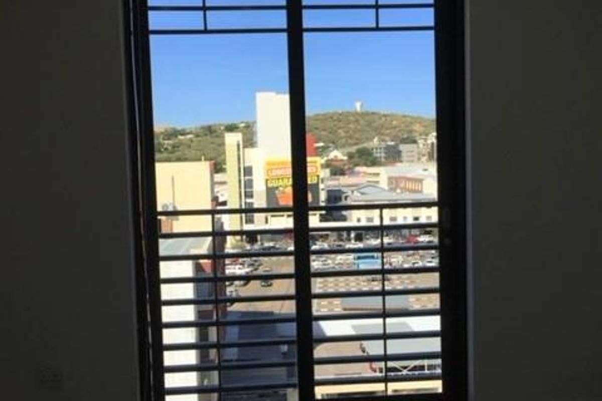 An empty living area featuring tiled flooring, track lighting, and a sliding glass door with an integrated security gate overlooking the city.