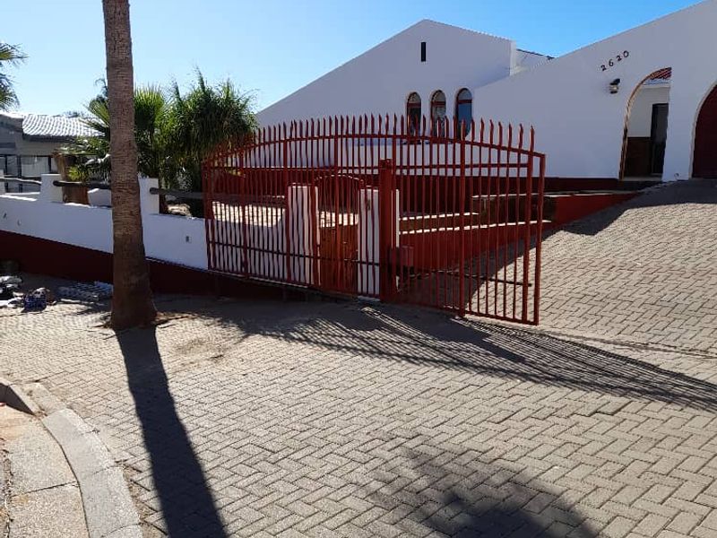 Front exterior view of the property featuring a paved driveway, secure metal gate, and white masonry facade with arched window details.