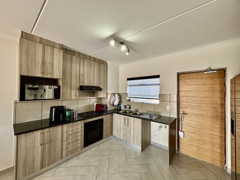 Modern kitchen featuring light wood-grain cabinetry, dark granite countertops, built-in oven and hob, and stylish herringbone floor tiling.