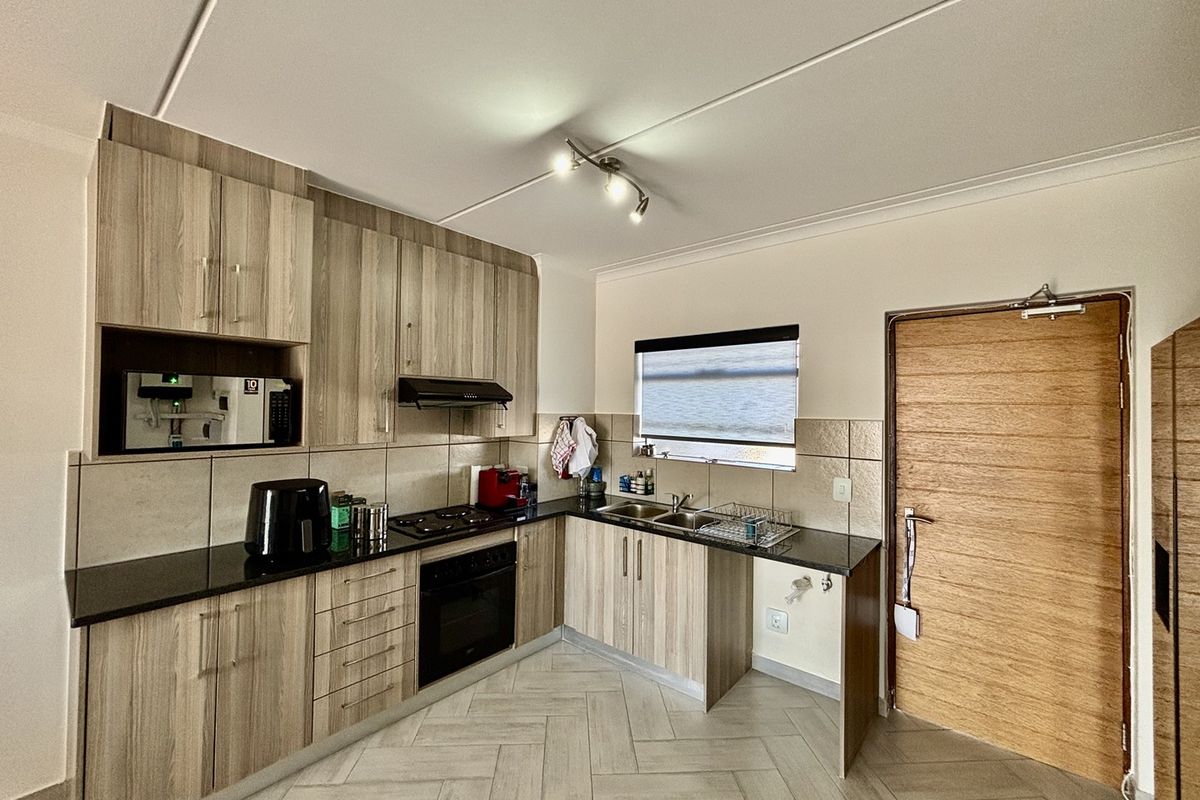 Modern kitchen featuring light wood-grain cabinetry, dark granite countertops, built-in oven and hob, and stylish herringbone floor tiling.