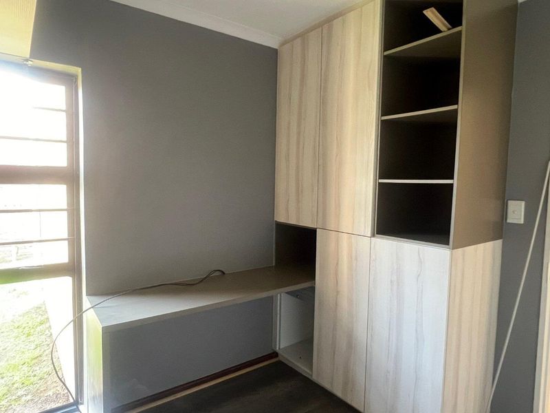 A functional home office space featuring modern built-in cabinetry, integrated desk workspace, and open shelving, finished with neutral grey walls.