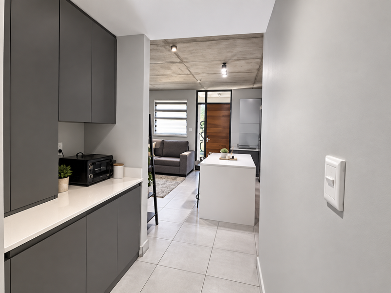 Modern open-plan living area featuring sleek grey cabinetry, stone countertops, a central kitchen island, and an industrial-style exposed concrete ceiling with tiled flooring.
