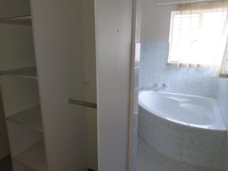 A dated bathroom featuring a corner bathtub with tiled surround and adjacent built-in storage shelving.