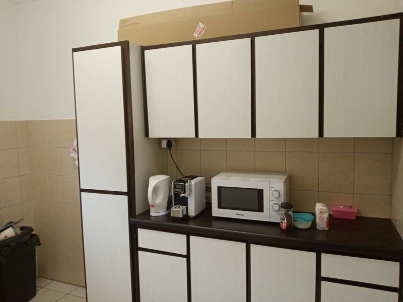 A functional office kitchenette featuring white cabinetry with dark trim, a tiled backsplash, and a laminate countertop with built-in microwave space.