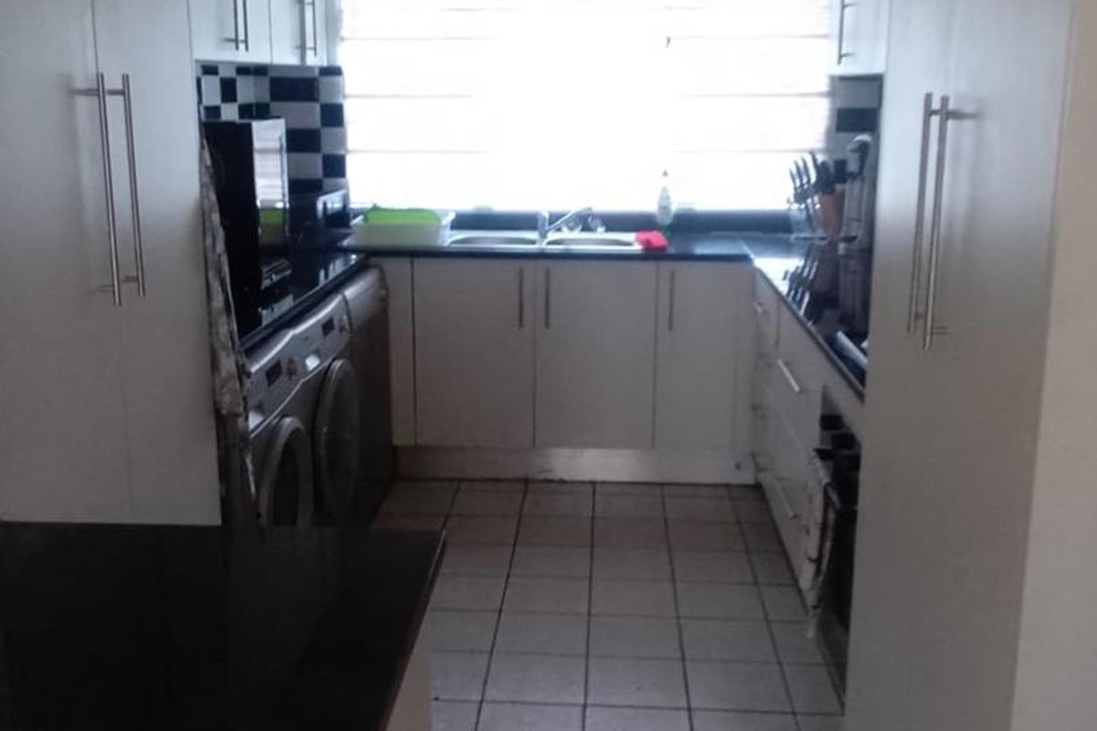 A functional galley-style kitchen featuring white cabinetry, dark countertops, tiled flooring, and integrated laundry appliances.