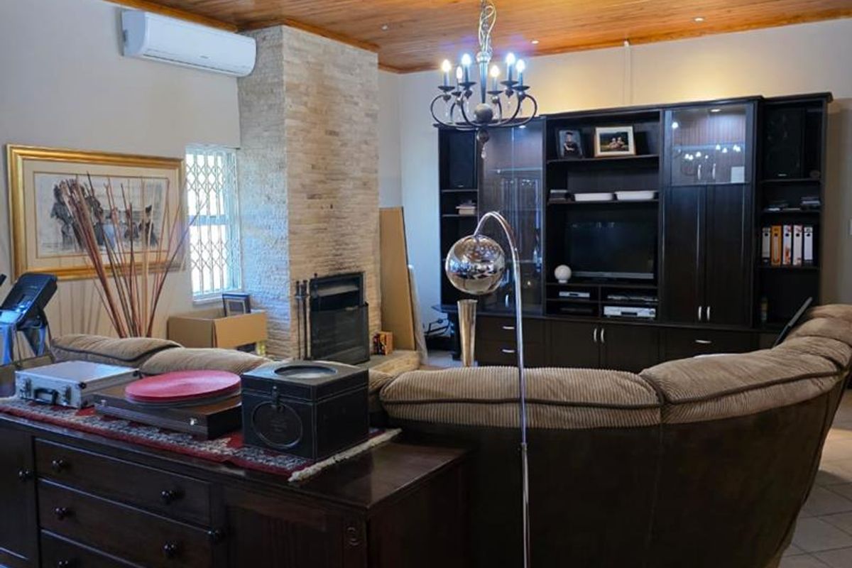 A living room featuring a wood-paneled ceiling, a stone-clad fireplace, and a built-in wall unit, complemented by tiled flooring and a wall-mounted air conditioning unit.