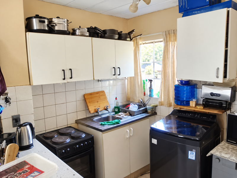 A compact kitchen featuring white cabinetry, a stainless steel sink, tiled backsplash, and an integrated electric stove, offering functional space for daily meal preparation.