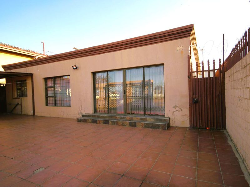 Rear exterior view featuring a tiled patio area, sliding glass doors with security gates, and a perimeter wall with security spikes.