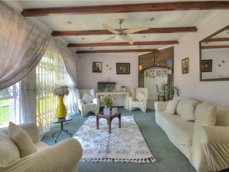 A living room featuring exposed timber ceiling beams, a ceiling fan, and a brick feature wall with access to the garden through sliding doors.