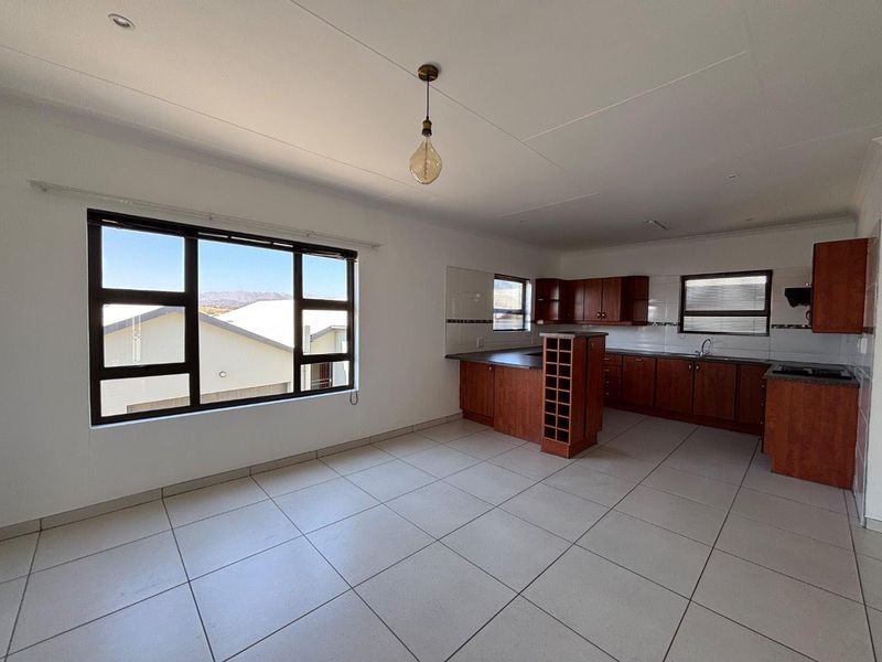 Spacious open-plan kitchen and living area featuring tiled floors, ample wooden cabinetry, and large windows providing natural light.
