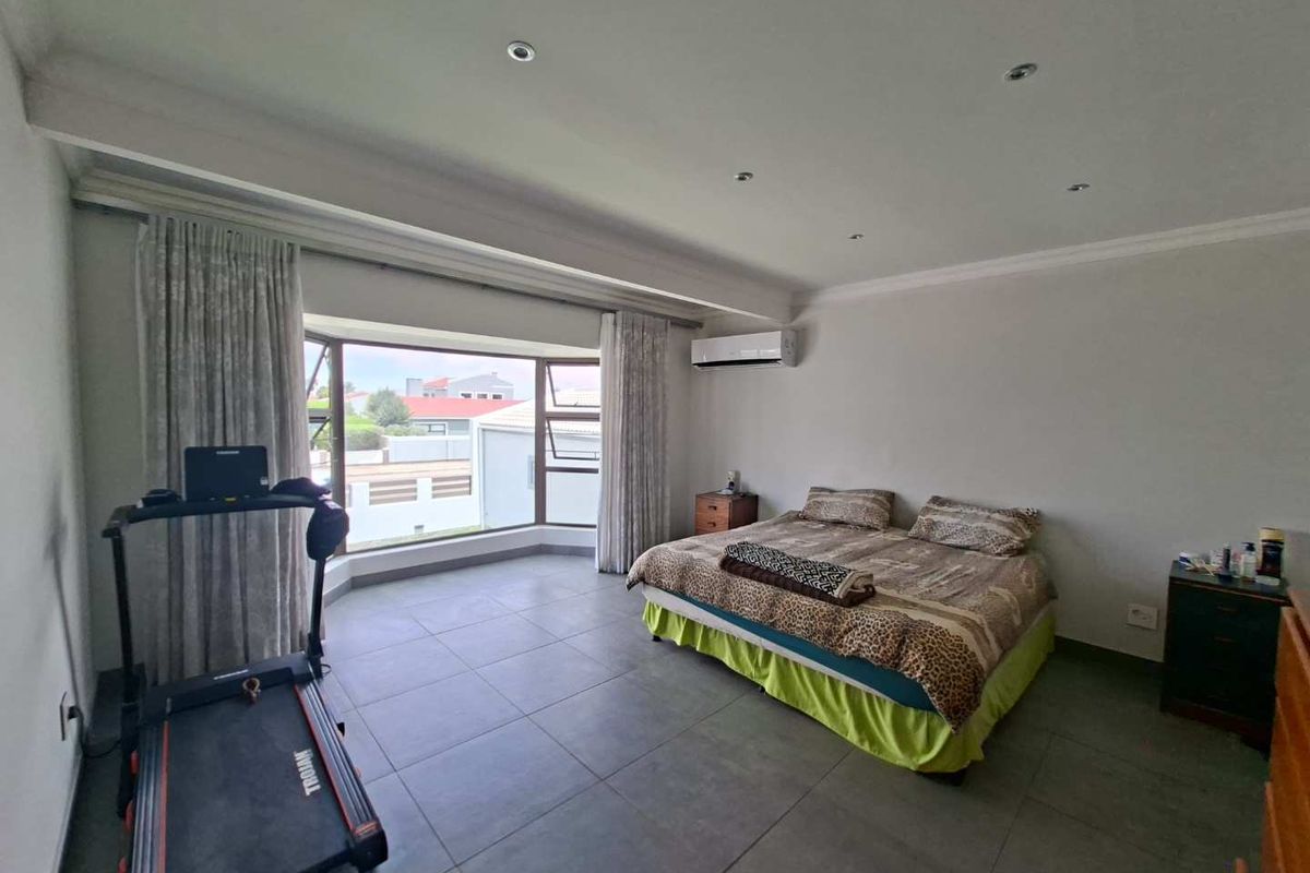 Spacious bedroom featuring large bay windows, tiled flooring, recessed downlighting, and a wall-mounted air conditioning unit.