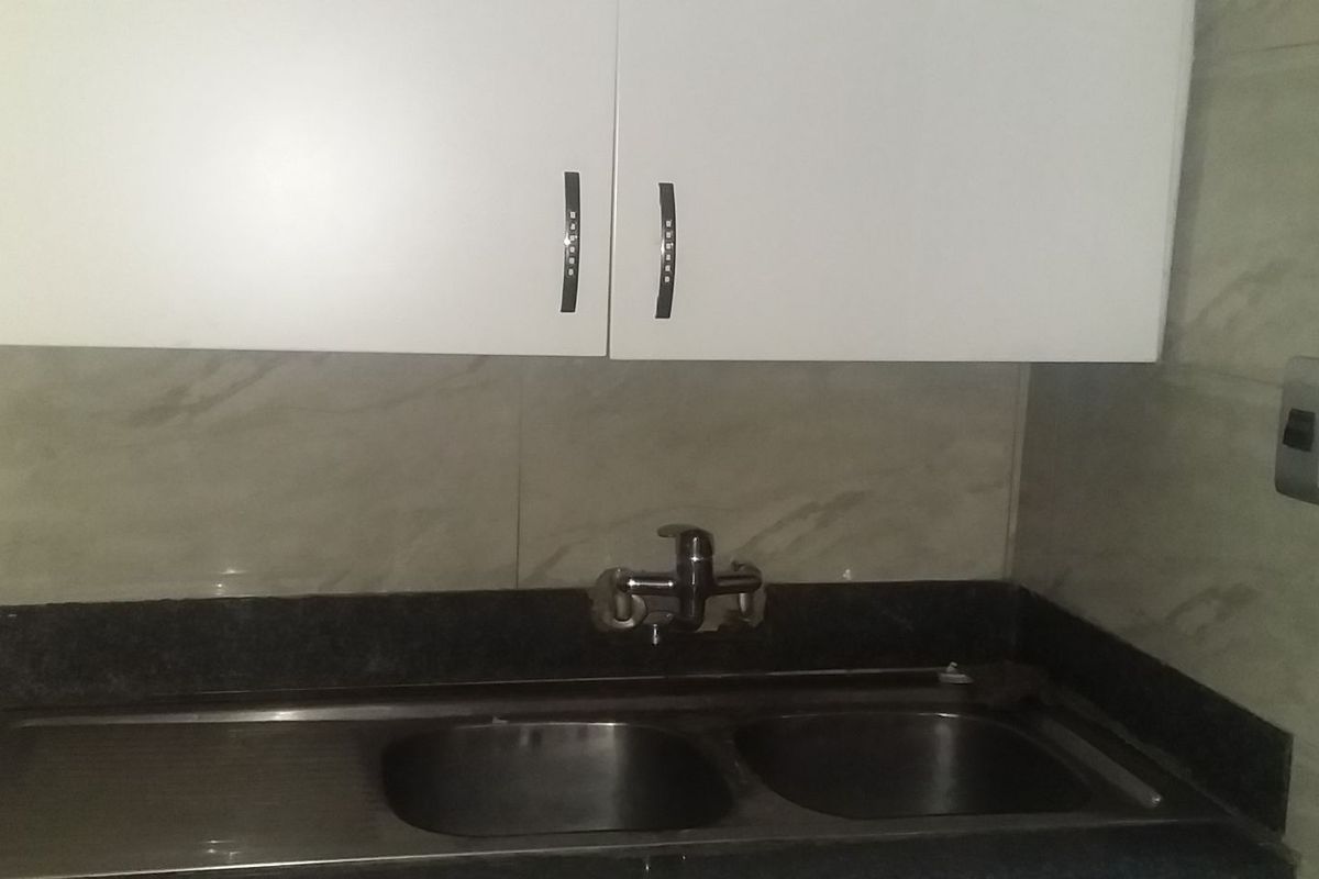A functional kitchen area featuring a double bowl stainless steel sink, granite countertop, and white overhead cabinetry with marble-effect wall tiling.