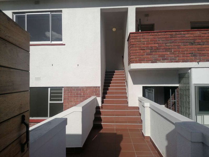 Exterior view of an apartment building entrance featuring a tiled staircase, brick balustrades, and a glass block feature wall.