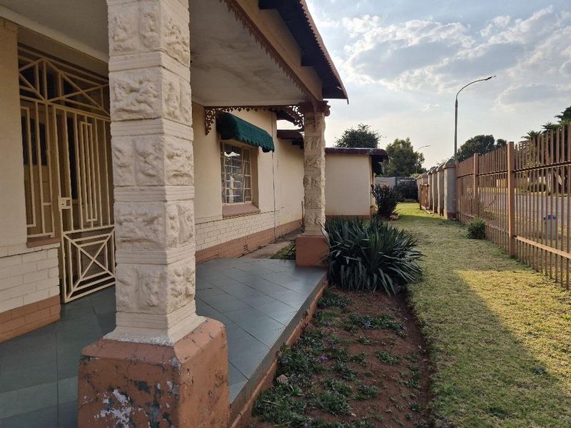 A covered patio area featuring decorative stone pillars, tiled flooring, and a metal security gate, overlooking a side garden and perimeter fencing.