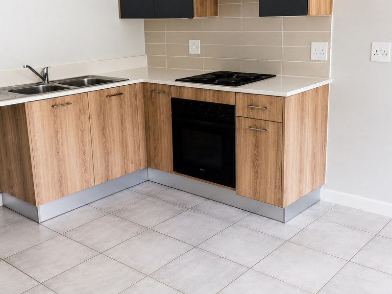 Modern kitchen featuring light wood-grain cabinetry, a built-in oven, electric hob, stainless steel sink, and neutral tiled flooring.