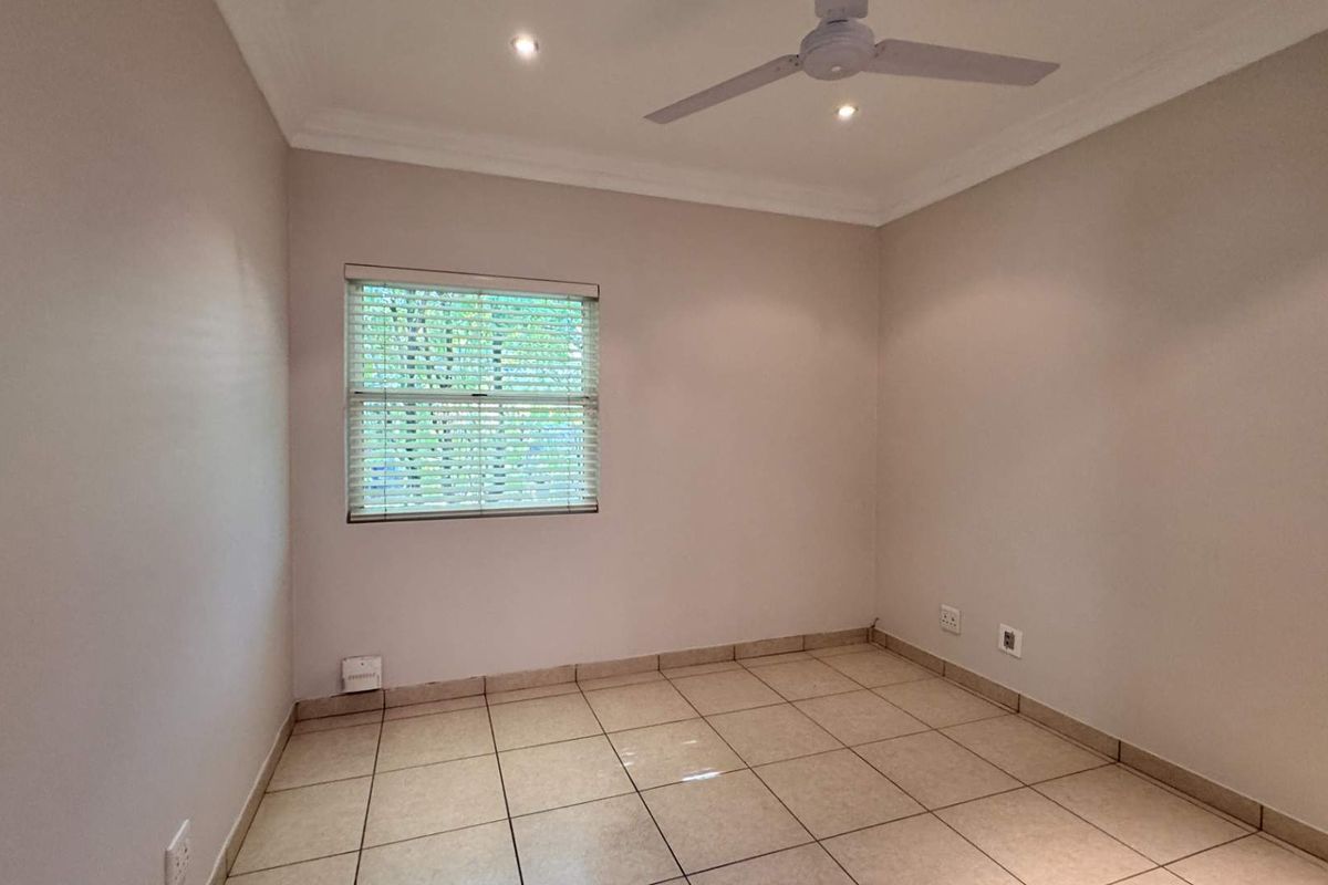 A clean, empty bedroom featuring neutral tiled flooring, a ceiling fan, recessed lighting, and venetian blinds.