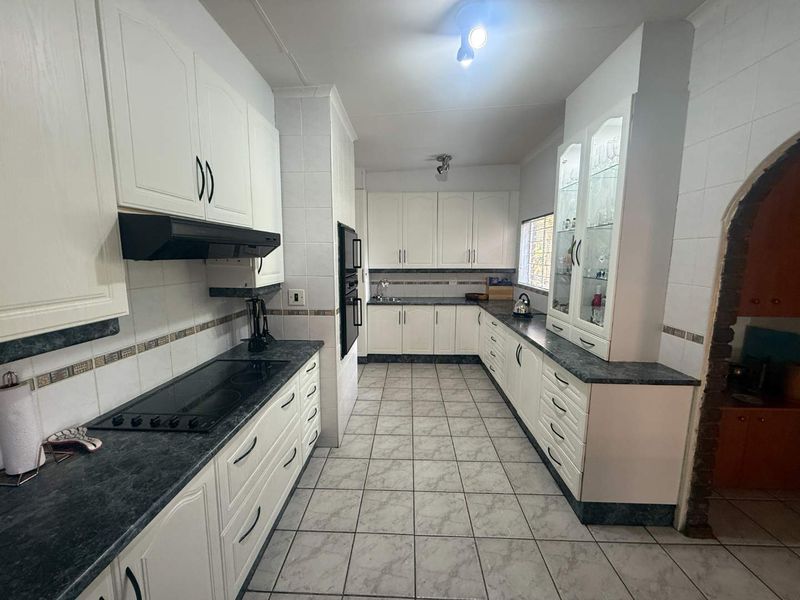 A functional kitchen featuring white cabinetry, dark laminate countertops, built-in oven, electric hob, and tiled finishes throughout.