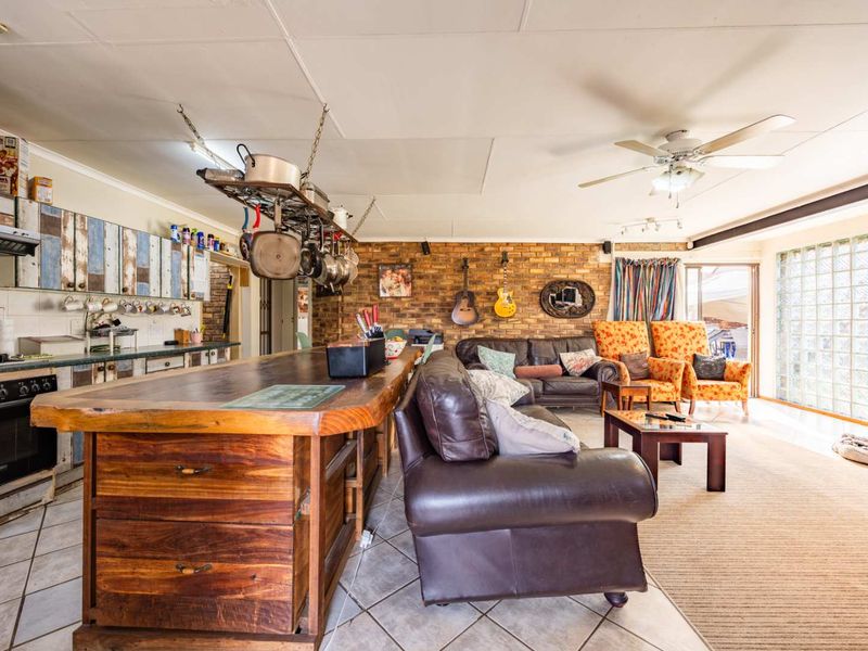 Open-plan living and kitchen area featuring an exposed brick wall, large timber kitchen island, ceiling fan, and unique glass block feature wall.