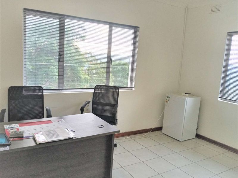 A functional office space featuring tiled flooring, large windows with venetian blinds, and neutral wall finishes, suitable for a professional work environment.