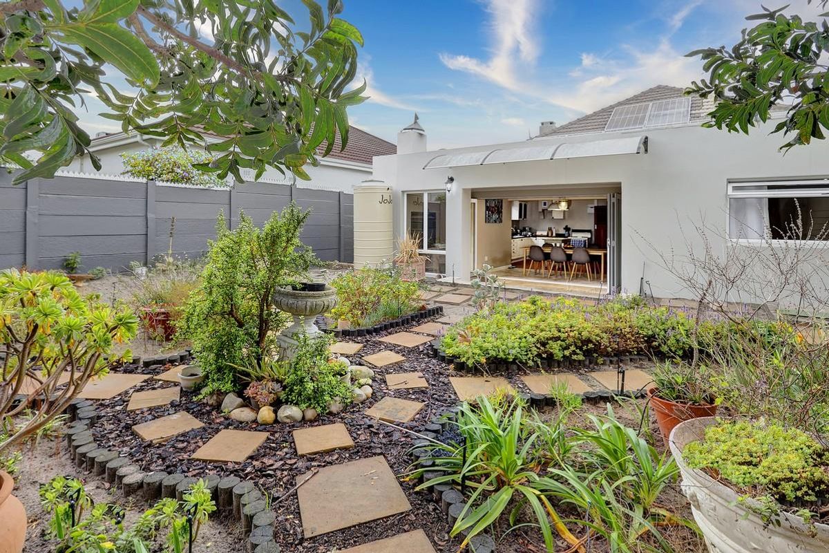 A well-maintained rear garden featuring a paved circular path, established landscaping, a water tank, and seamless indoor-outdoor flow through bi-fold doors.
