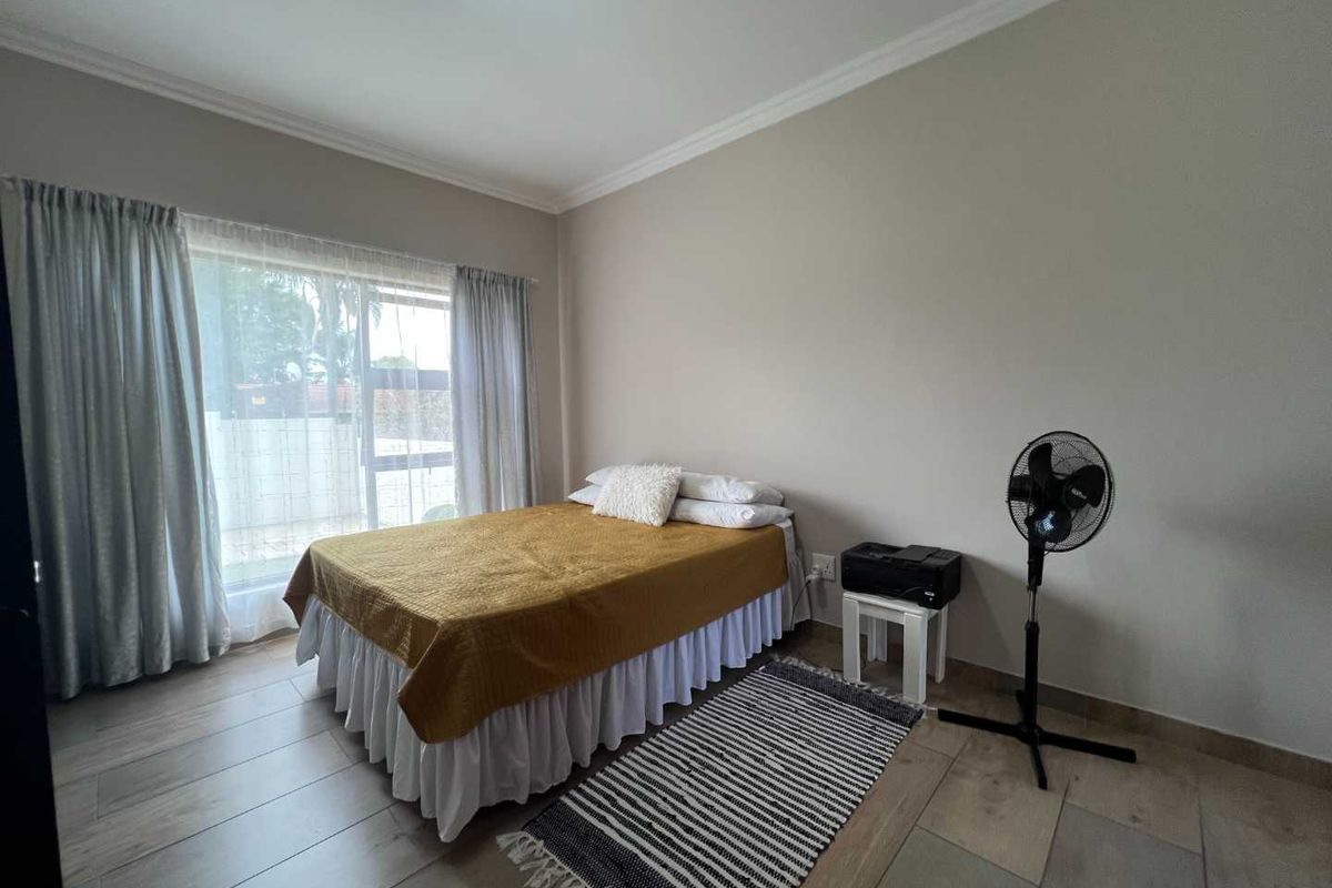 A well-lit bedroom featuring neutral wall tones, tiled flooring, and large windows with curtains, providing a clean and functional living space.
