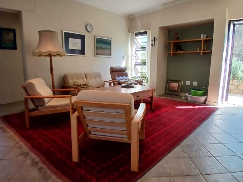 A spacious living room featuring tiled flooring, recessed lighting, and a built-in shelving alcove, with direct access to an outdoor area via a sliding door.