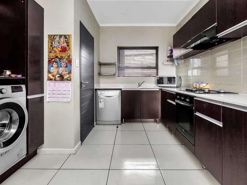 Modern kitchen featuring dark wood cabinetry, tiled flooring, built-in oven, hob, extractor fan, and integrated space for laundry appliances.