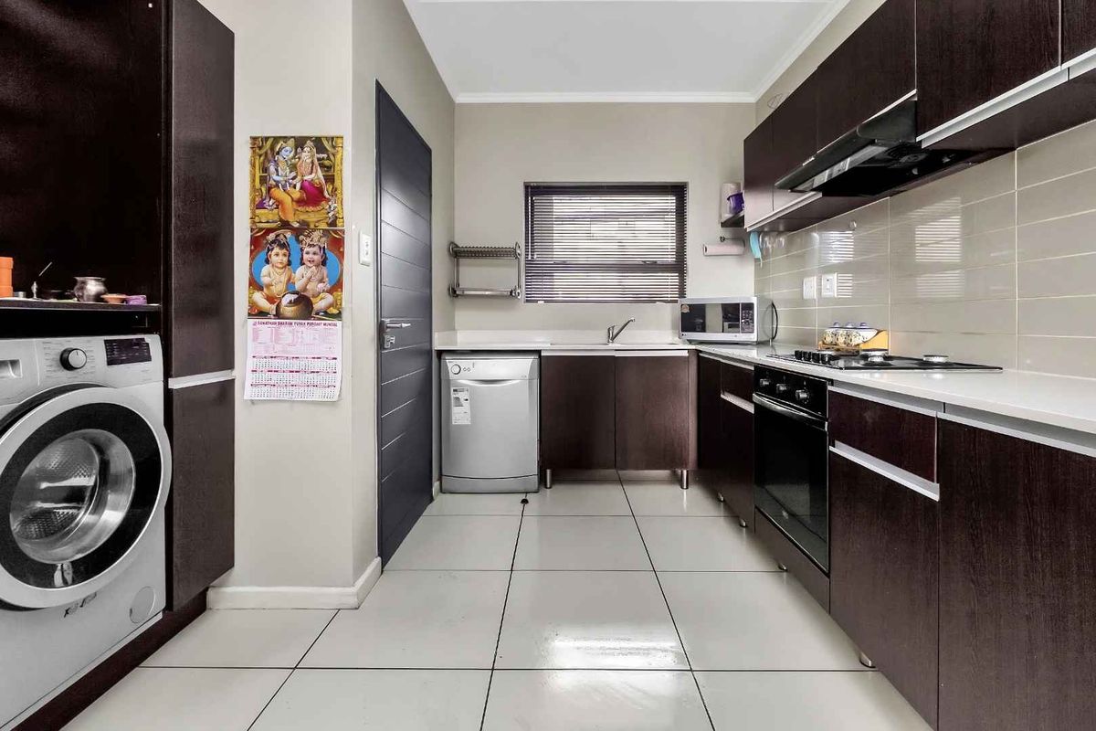 Modern kitchen featuring dark wood cabinetry, tiled flooring, built-in oven, hob, extractor fan, and integrated space for laundry appliances.