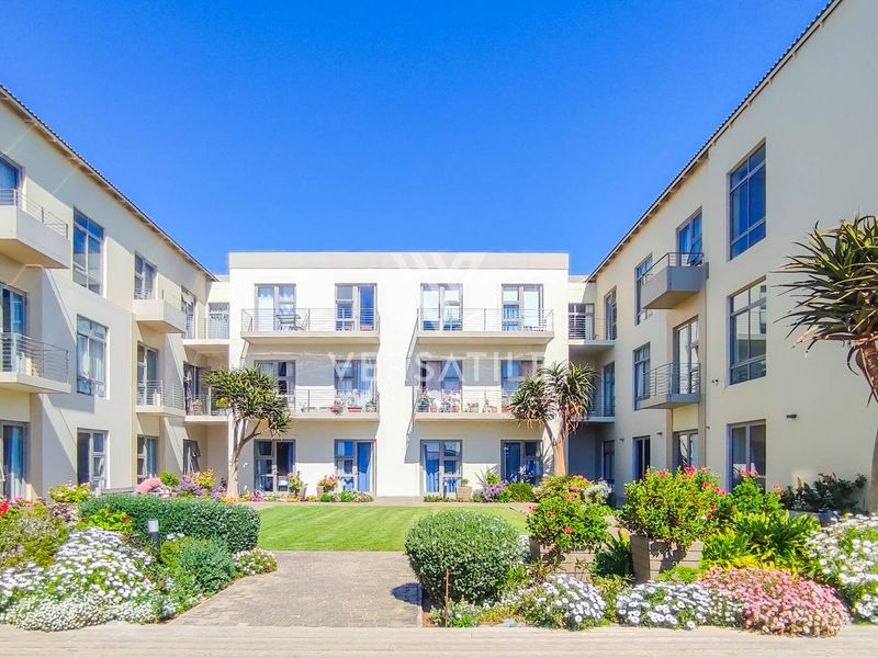 A well-maintained central courtyard garden featuring a paved walkway, manicured lawn, and surrounding apartment blocks with private balconies.