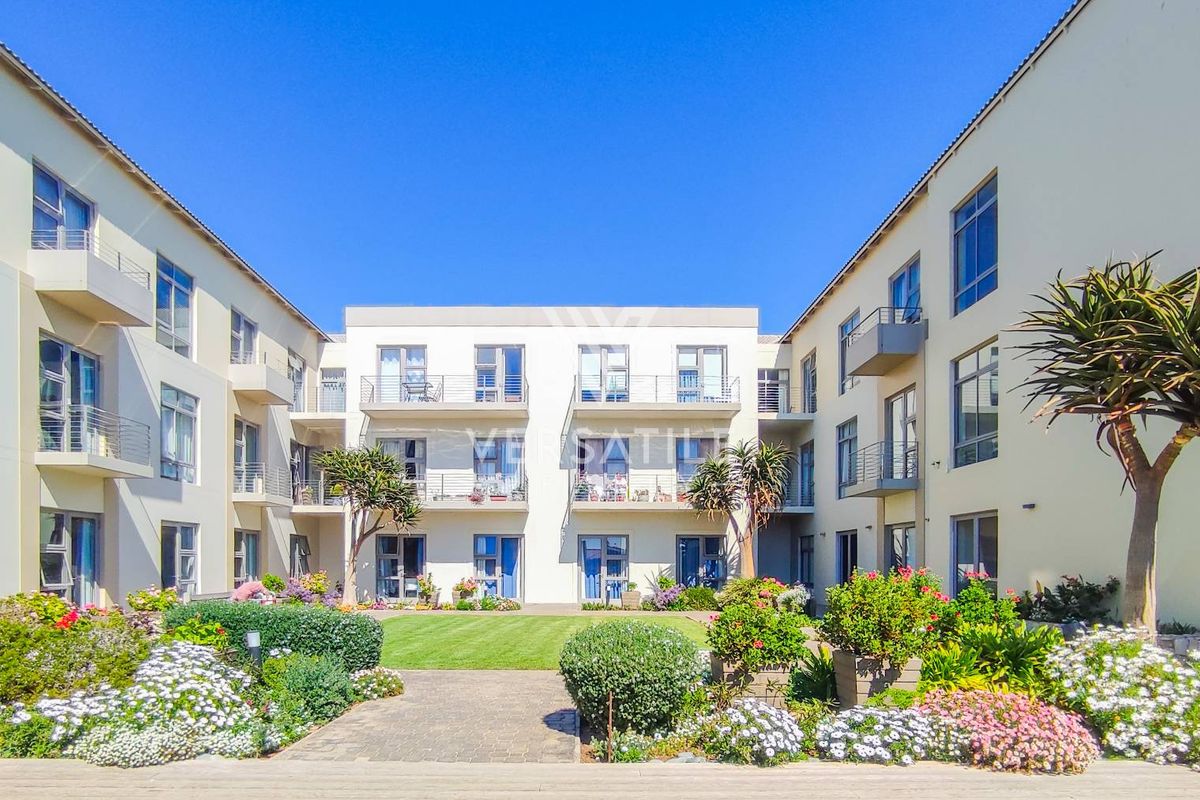 A well-maintained central courtyard garden featuring a paved walkway, manicured lawn, and surrounding apartment blocks with private balconies.