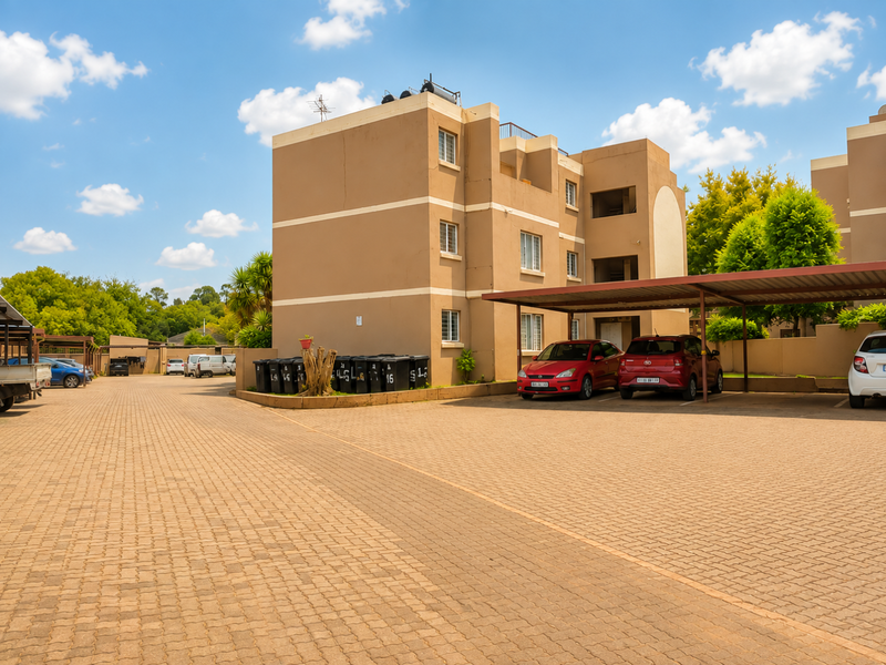 Exterior view of a multi-story townhouse complex featuring a paved parking area, covered carports, and communal waste disposal facilities.
